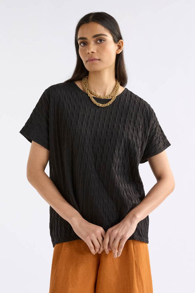 Woman wearing a black textured top and orange pants on a white background by Elk the Label | Elk Stockist in Newcastle, NSW at Zebra Finch Style