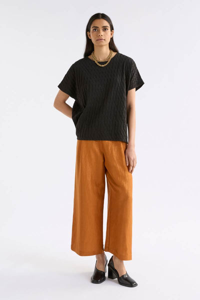 Woman wearing a black t-shirt and orange pants on a white background Woman wearing a black textured top and orange pants on a white background by Elk the Label | Elk Stockist in Newcastle, NSW at Zebra Finch Style