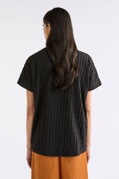 Person wearing a black textured shirt and orange pants on a white background Woman wearing a black textured top and orange pants on a white background by Elk the Label | Elk Stockist in Newcastle, NSW at Zebra Finch Style