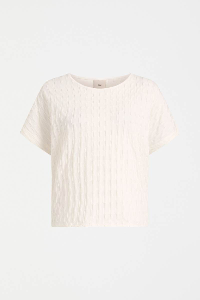 White textured t-shirt on a light gray background Woman wearing a white textured top and gray pants on a light background by Elk the Label | Elk Stockist in Newcastle, NSW at Zebra Finch Style