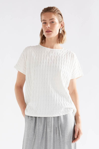 Woman wearing a white textured top and gray pants on a light background by Elk the Label | Elk Stockist in Newcastle, NSW at Zebra Finch Style