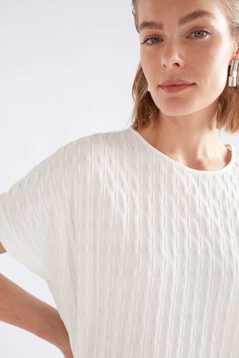 Woman wearing a white textured top against a light background Woman wearing a white textured top and gray pants on a light background by Elk the Label | Elk Stockist in Newcastle, NSW at Zebra Finch Style