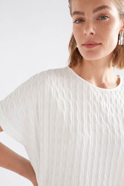 Woman wearing a white textured top against a light background Woman wearing a white textured top and gray pants on a light background by Elk the Label | Elk Stockist in Newcastle, NSW at Zebra Finch Style