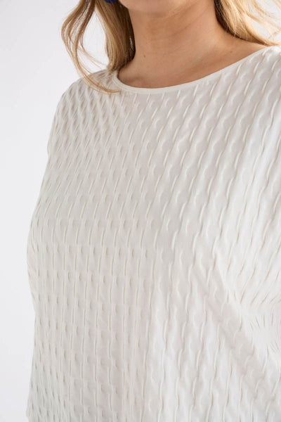 Close-up of a person wearing a textured white top against a white background Woman wearing a white textured top and gray pants on a light background by Elk the Label | Elk Stockist in Newcastle, NSW at Zebra Finch Style
