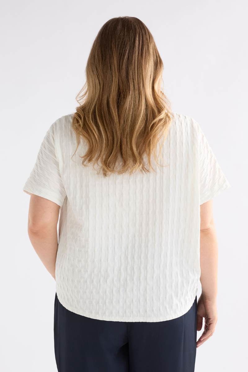 Person wearing a textured white shirt and dark pants on a light background Woman wearing a white textured top and gray pants on a light background by Elk the Label | Elk Stockist in Newcastle, NSW at Zebra Finch Style