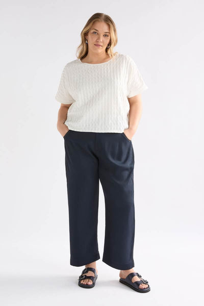Woman wearing a white top and navy pants on a white background Woman wearing a white textured top and gray pants on a light background by Elk the Label | Elk Stockist in Newcastle, NSW at Zebra Finch Style