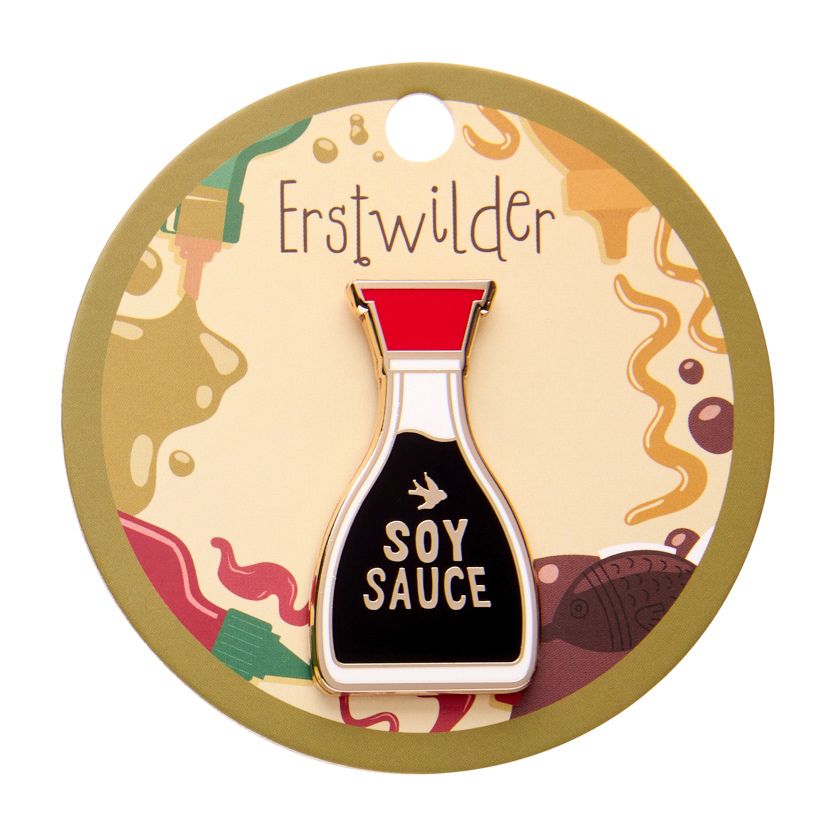 Pin shaped like a soy sauce bottle with red cap and black body on a white background. Erstwilder's soy sauce brooch from their 2025 condiments collection