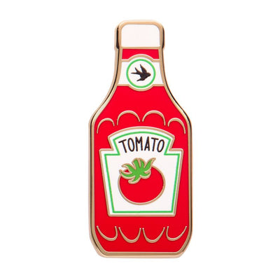 Enamel pin shaped like a tomato ketchup bottle with a logo on a white background. Erstwilder's Tomato sauce enamel pin from their 2025 Condiments collection