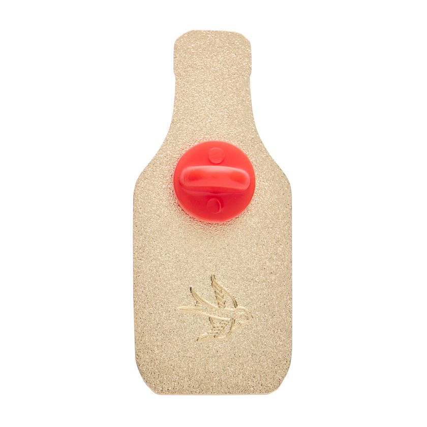 Enamel pin shaped like a tomato ketchup bottle with a logo on a white background. Erstwilder's Tomato sauce enamel pin from their 2025 Condiments collection