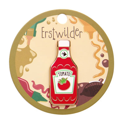 Enamel pin shaped like a tomato ketchup bottle with a logo on a white background. Erstwilder's Tomato sauce enamel pin from their 2025 Condiments collection