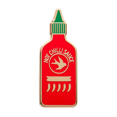 Hot chilli sauce bottle-shaped enamel pin with red body, green cap, and gold accents on a white background. Erstwilder's chilli enamel pin from their 2025 Condiments collection