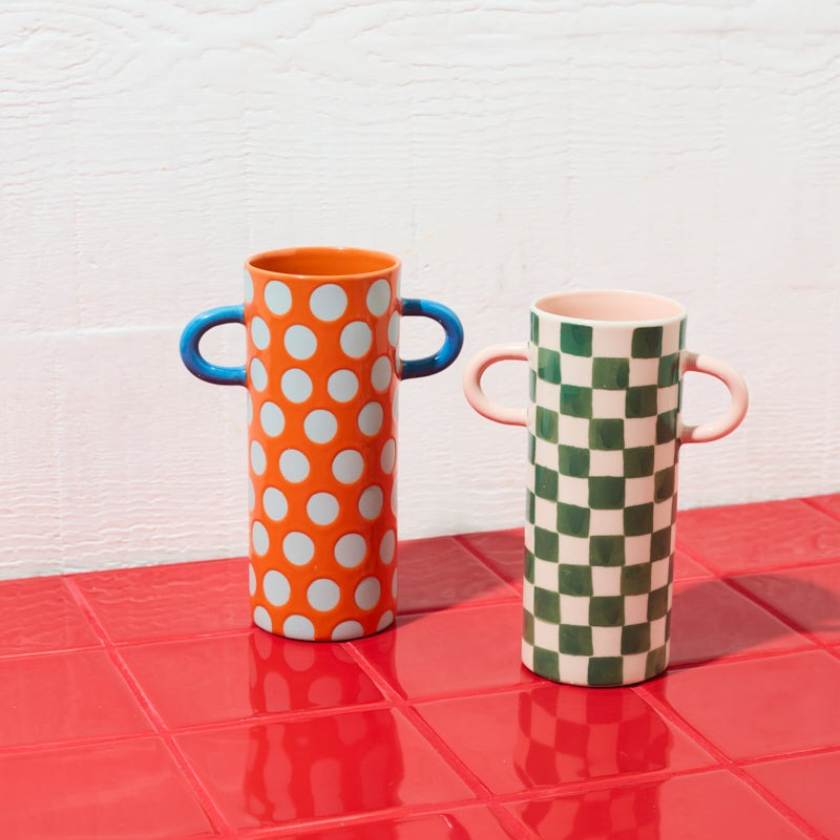 Two colorful vases with handles on a red surface against a white wall.