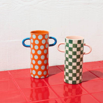 Two colorful vases with handles on a red surface against a white wall.