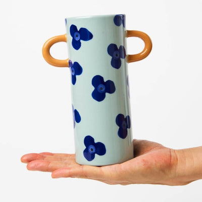 Ceramic vase with blue floral pattern and brown handles held in a hand against a white background