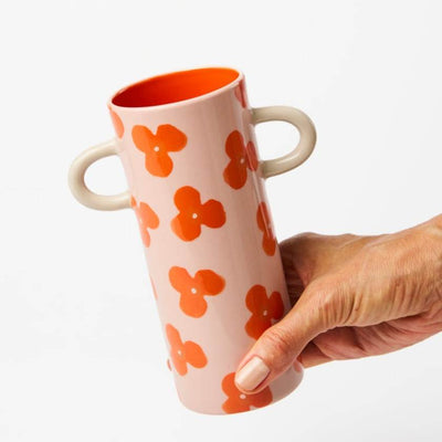 Hand holding a pink vase with orange floral patterns on a white background