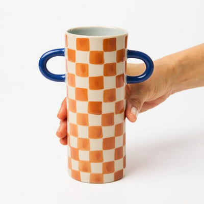 Checkered vase with blue handles held by a hand on a white background