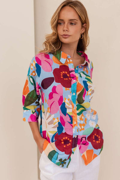 Woman wearing a colourful floral shirt against a beige background. Shirt by Kaleido - Kaleido Stockist at Zebra Finch in Newcastle, NSW
