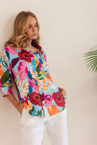 Woman wearing a colourful floral shirt against a beige background. Shirt by Kaleido - Kaleido Stockist at Zebra Finch in Newcastle, NSW