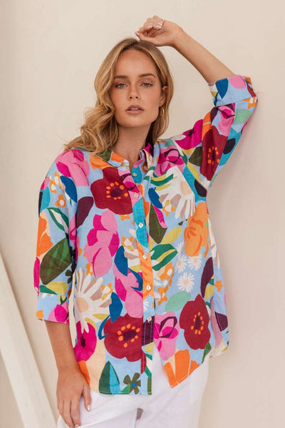 Woman wearing a colourful floral shirt against a beige background. Shirt by Kaleido - Kaleido Stockist at Zebra Finch in Newcastle, NSW