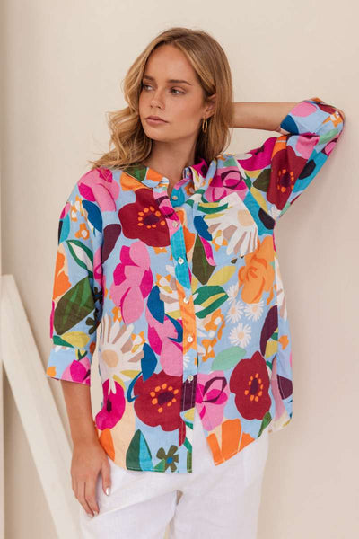 Woman wearing a colourful floral shirt against a beige background. Shirt by Kaleido - Kaleido Stockist at Zebra Finch in Newcastle, NSW