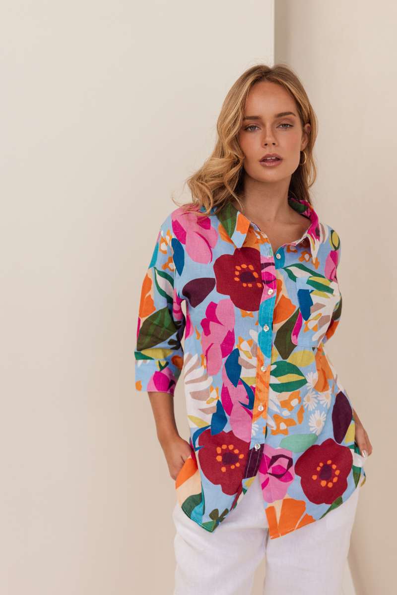 Woman wearing a colourful floral shirt against a beige background. Shirt by Kaleido - Kaleido Stockist at Zebra Finch in Newcastle, NSW