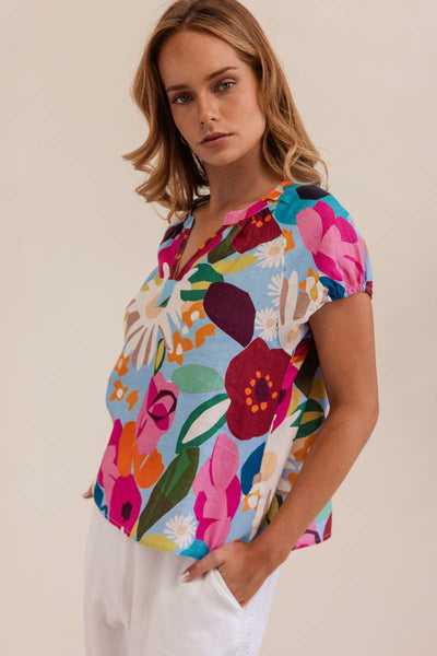 Woman wearing a colorful floral blouse against a beige background. Kaleido linen blouse- stockist at Zebra Finch Marketown in Newcastle, NSW