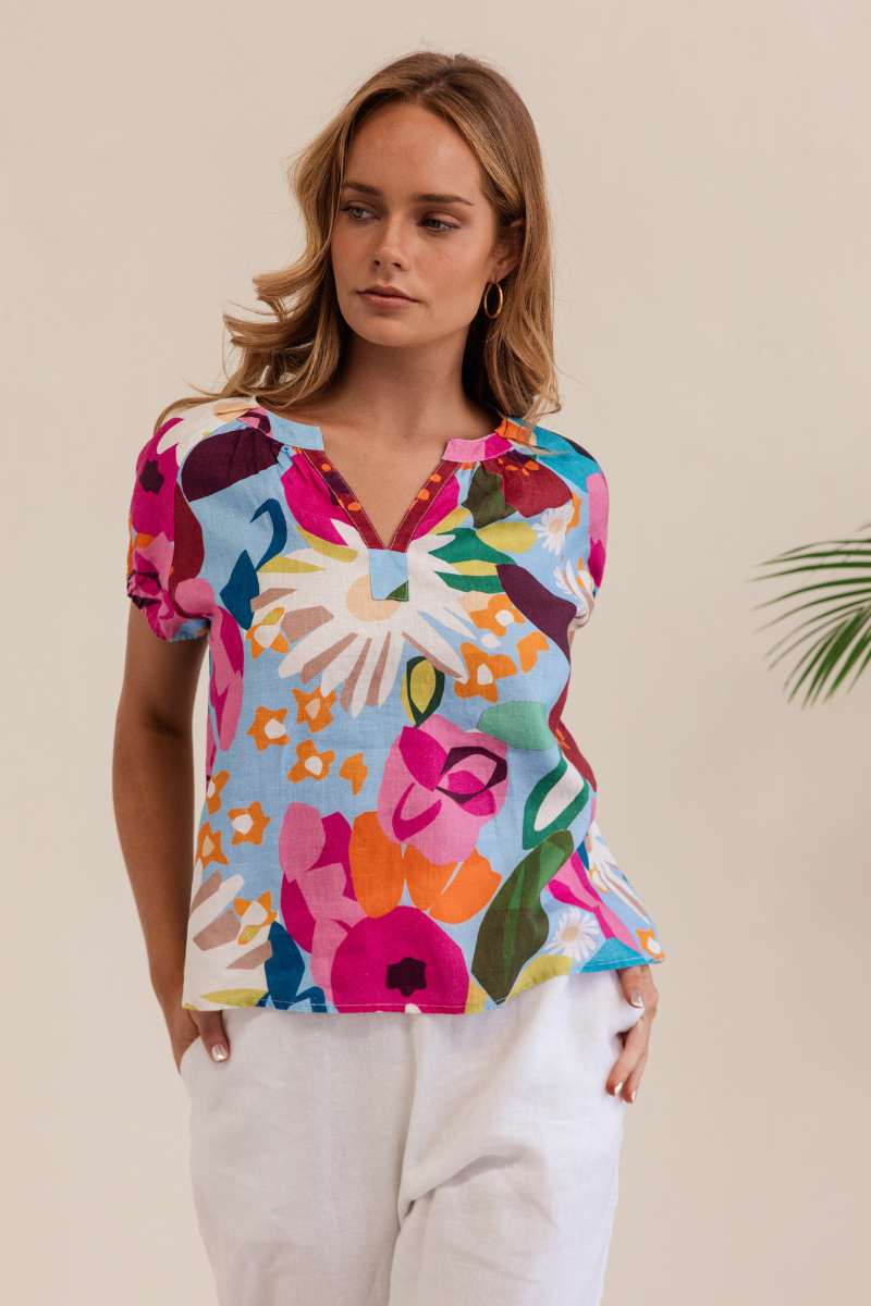 Woman wearing a colorful floral blouse against a beige background. Kaleido linen blouse- stockist at Zebra Finch Marketown in Newcastle, NSW