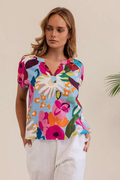 Woman wearing a colorful floral blouse against a beige background. Kaleido linen blouse- stockist at Zebra Finch Marketown in Newcastle, NSW