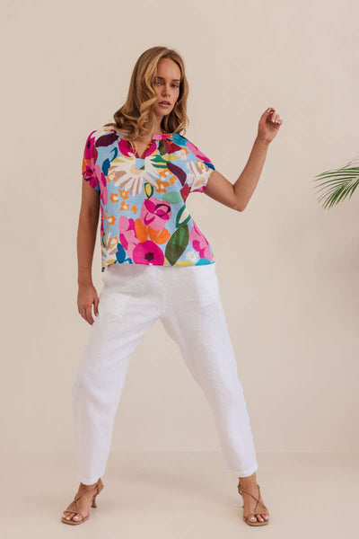 Woman wearing a colorful floral blouse against a beige background. Kaleido linen blouse- stockist at Zebra Finch Marketown in Newcastle, NSW