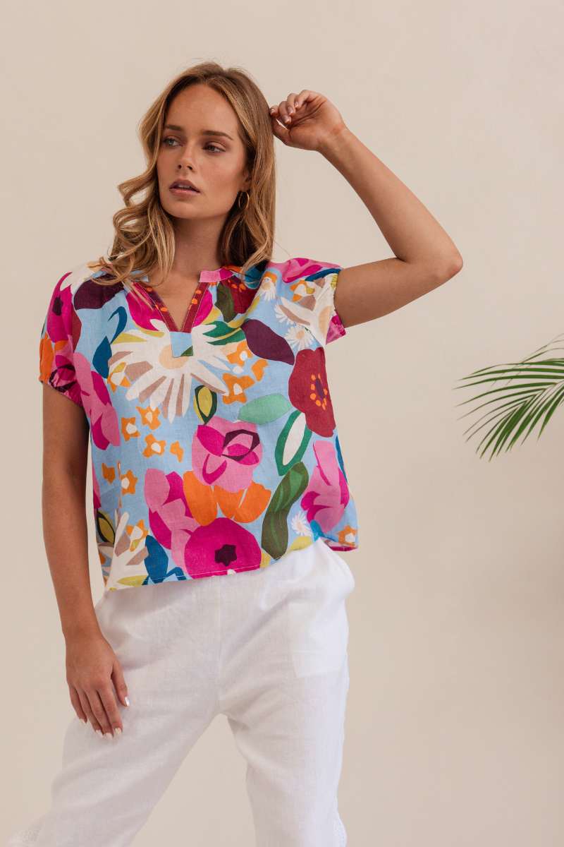 Woman wearing a colorful floral blouse against a beige background. Kaleido linen blouse- stockist at Zebra Finch Marketown in Newcastle, NSW