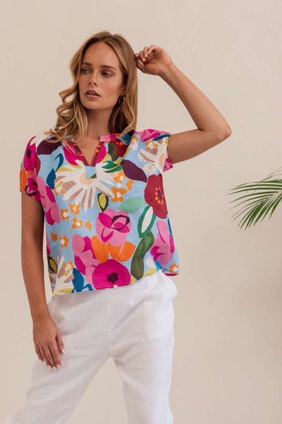 Woman wearing a colorful floral blouse against a beige background. Kaleido linen blouse- stockist at Zebra Finch Marketown in Newcastle, NSW