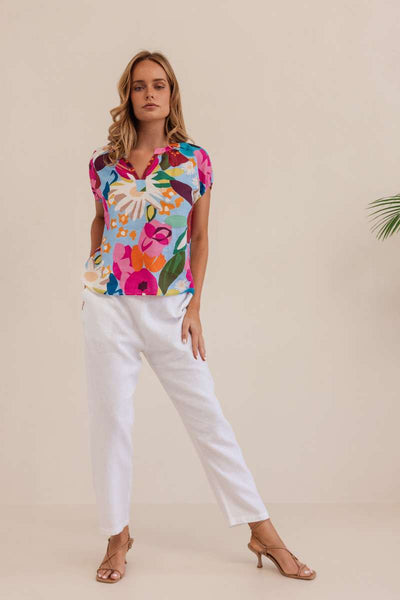 Woman wearing a colorful floral blouse against a beige background. Kaleido linen blouse- stockist at Zebra Finch Marketown in Newcastle, NSW