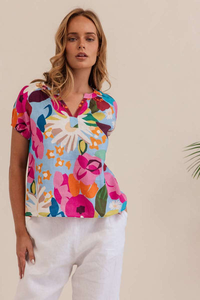 Woman wearing a colorful floral blouse against a beige background. Kaleido linen blouse- stockist at Zebra Finch Marketown in Newcastle, NSW
