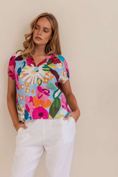 Woman wearing a colorful floral blouse against a beige background. Kaleido linen blouse- stockist at Zebra Finch Marketown in Newcastle, NSW