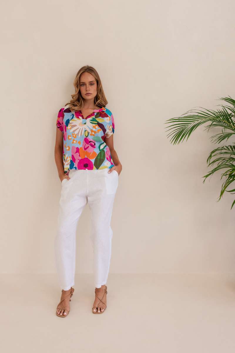 Woman wearing a colorful floral blouse against a beige background. Kaleido linen blouse- stockist at Zebra Finch Marketown in Newcastle, NSW