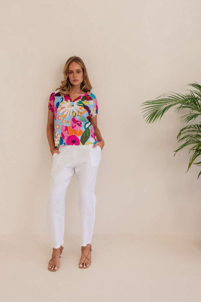 Woman wearing a colorful floral blouse against a beige background. Kaleido linen blouse- stockist at Zebra Finch Marketown in Newcastle, NSW