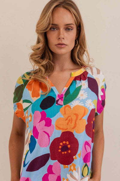 Woman wearing a colorful floral blouse against a beige background. Kaleido linen blouse- stockist at Zebra Finch Marketown in Newcastle, NSW