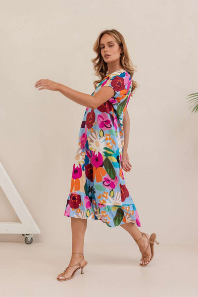 Woman wearing a colourful floral dress against a plain background. Dress by Kaleido. Kaleido Stockist in Newcastle, NSW at Zebra Finch