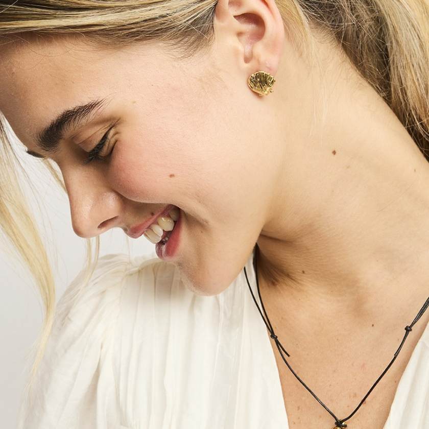 Close-up of a woman wearing gold earrings and a black necklace against a neutral background by Tiger Tree