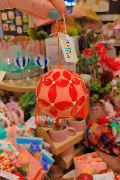 Decorative red and white ball ornament with a tag in a store setting by Mink and Me