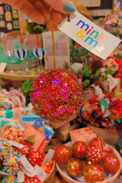 Decorative ball with colorful beads held by a hand, with a 'mink and me' tag in a store setting.