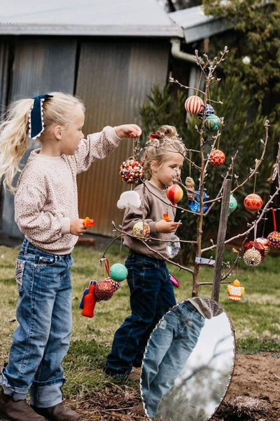 Two children playing with Christmas ornaments on a tree in an outdoor setting.
