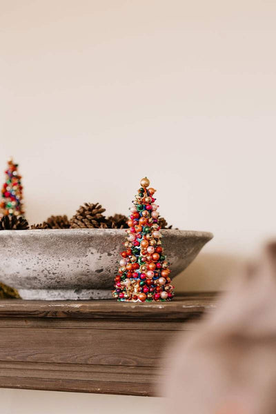 Decorative Christmas trees with colorful beads in a concrete bowl on a wooden surface.