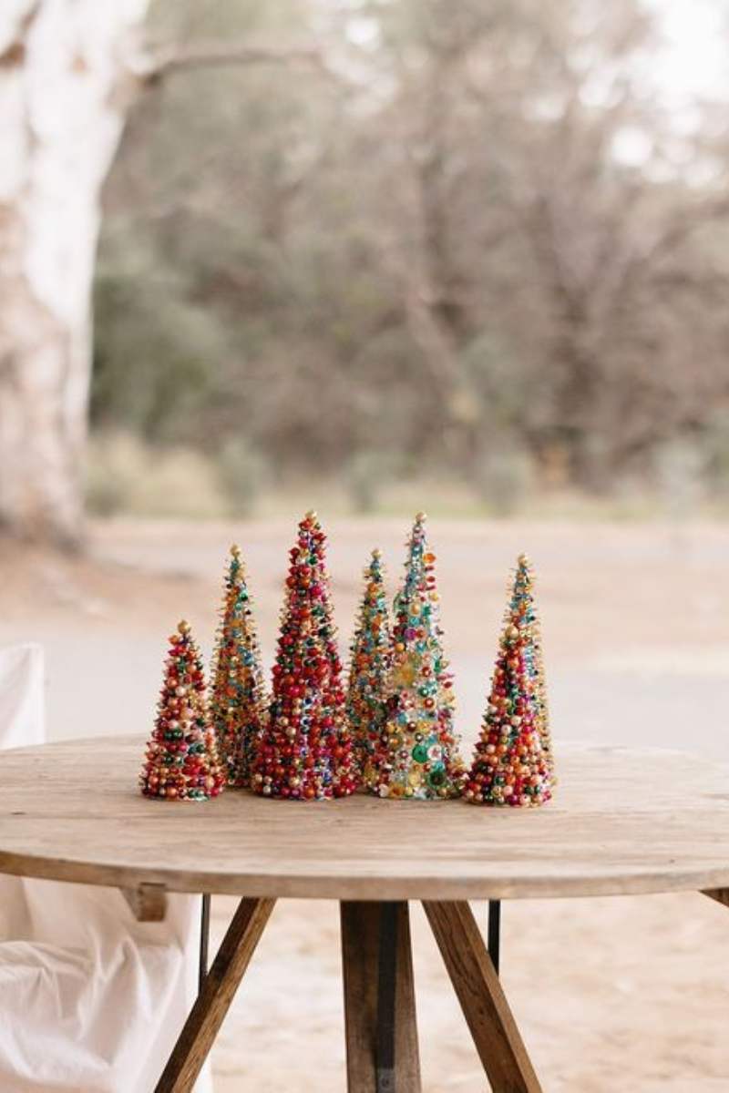 Colorful miniature Christmas trees on a wooden table with a blurred natural background