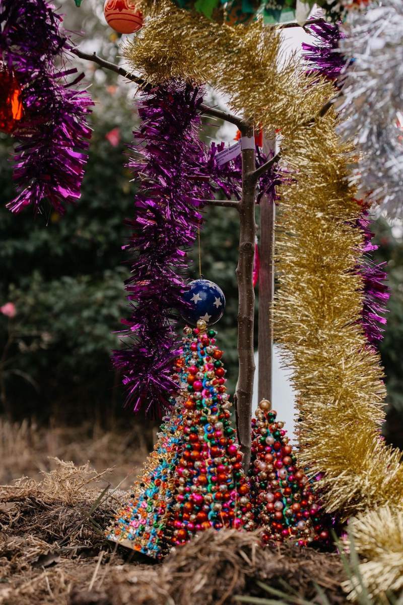 Decorative Christmas tree made of colorful beads with tinsel and ornaments in the background.