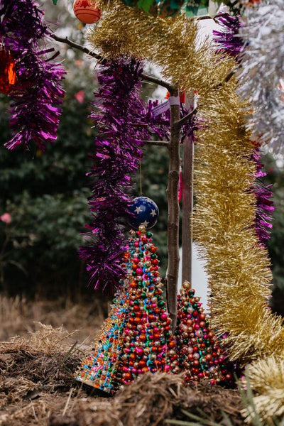 Decorative Christmas tree made of colorful beads with tinsel and ornaments in the background.