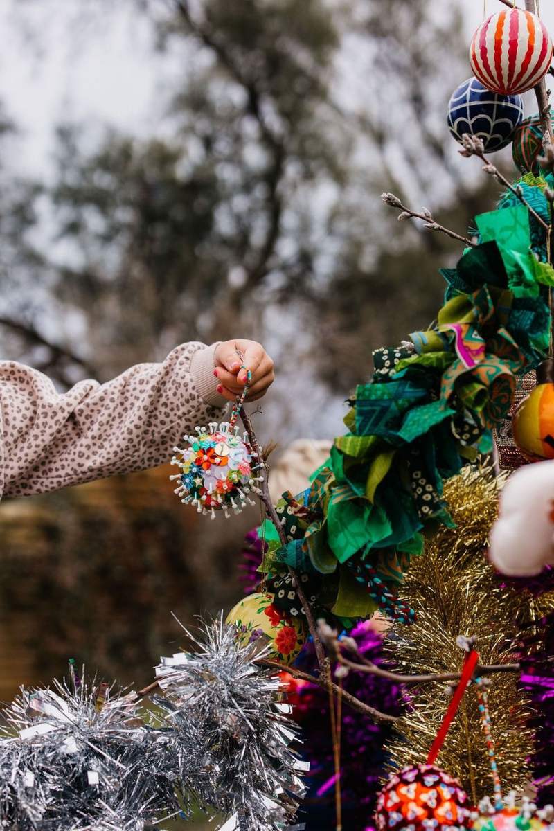 Decorative wreath with colorful ornaments and a child's hand holding one, against a natural background.
