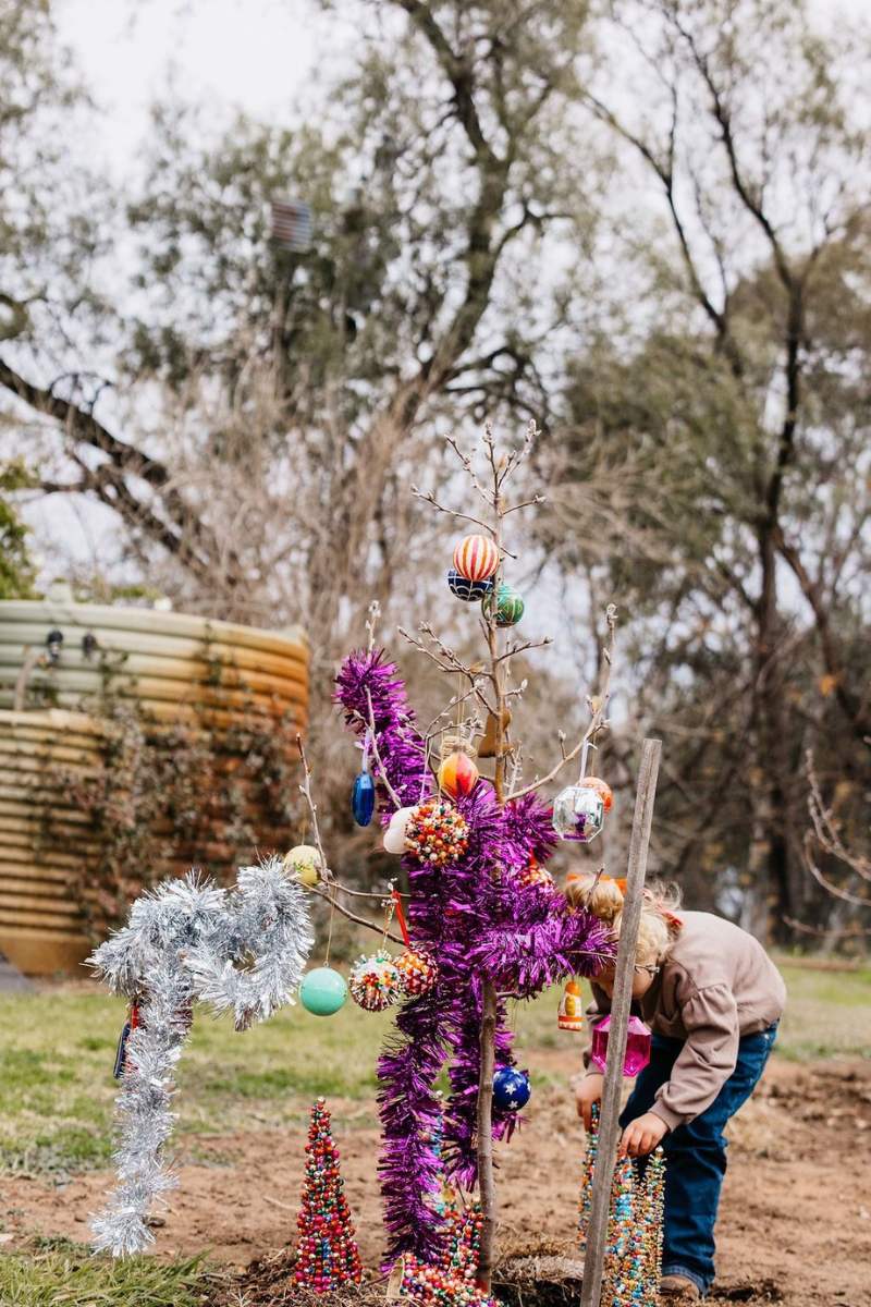 Person decorating a tree with colorful ornaments in an outdoor setting