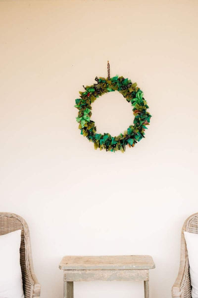 Green wreath hanging on a white wall with two wicker chairs and a small table. by Mink and Me