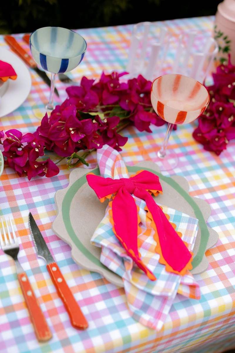 Colorful table setting with plaid tablecloth, pink napkin, and vibrant flowers.
